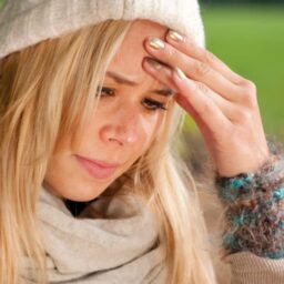 woman with a red nose putting her hand to her forehead in pain