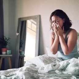 Woman in bed blowing her nose.