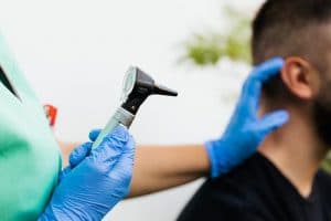 Doctor or nurse preparing to give man an ear exam.