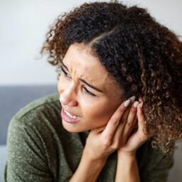 Woman experiencing ear pain, holding her hand up to her ear.
