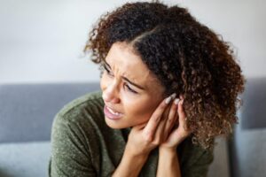 Woman experiencing ear pain, holding her hand up to her ear.