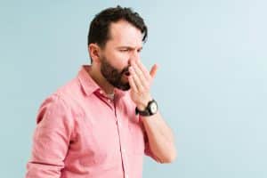 Man in a pink shirt checking to see if his breath smells bad.
