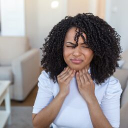 Young woman wincing and touching her throat.