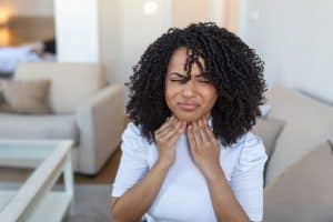 Young woman wincing and touching her throat.