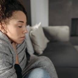Woman feeling ill, wrapped up in a blanket and resting at home.