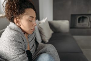 Woman feeling ill, wrapped up in a blanket and resting at home.