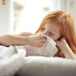 Little girl blowing her nose in bed.