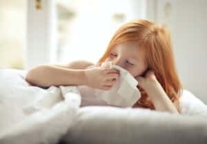 Little girl blowing her nose in bed.