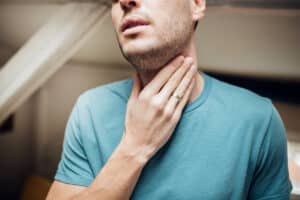 Close-up of a man touching his sore throat.