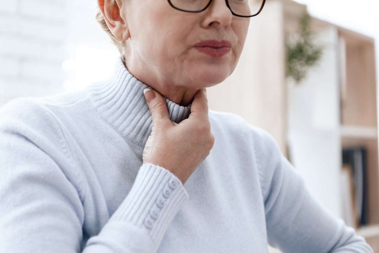 Woman holds hand on throat
